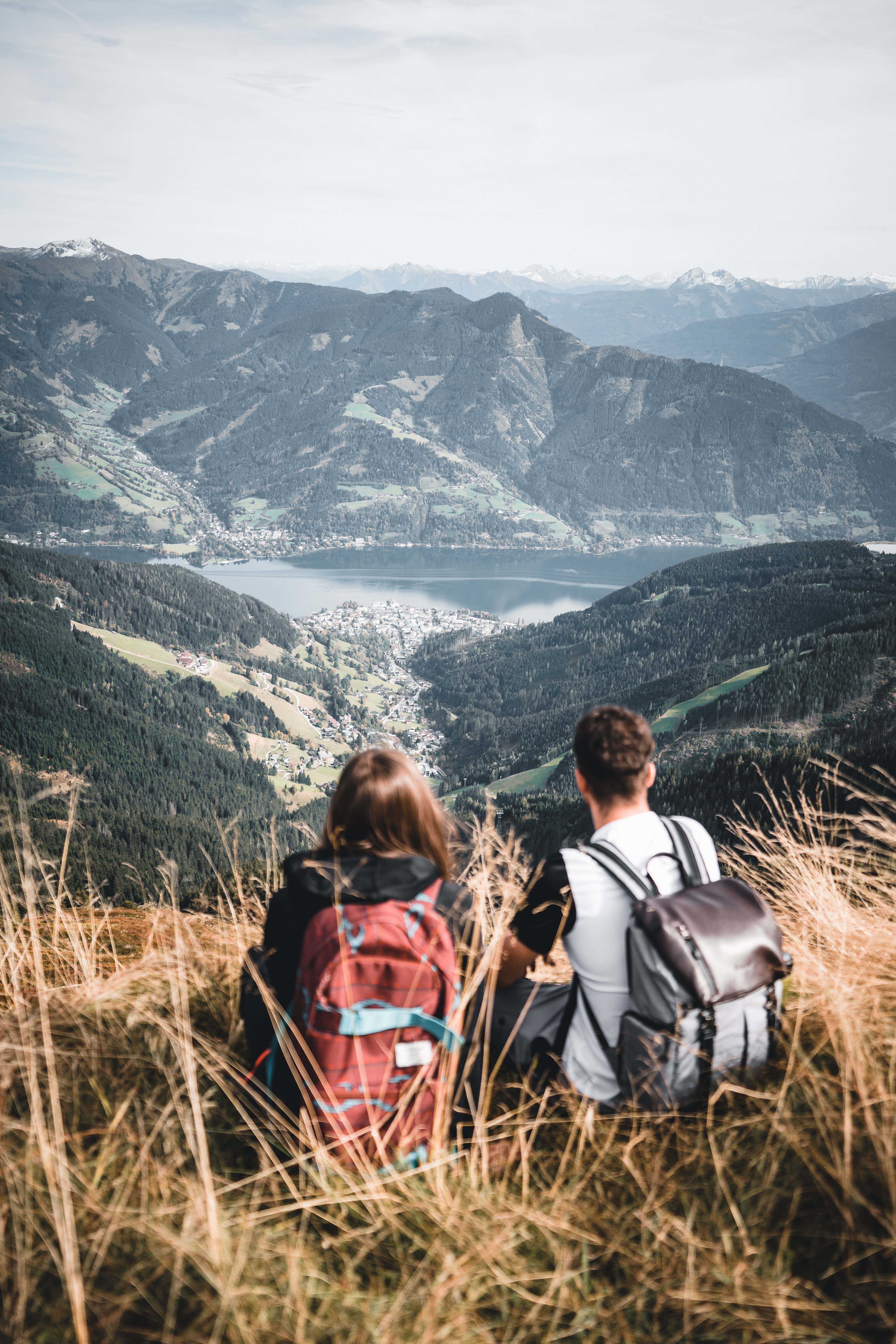 Zwei Wanderer mit Rucksäcken blicken auf Zell am See und Alpenpanorama